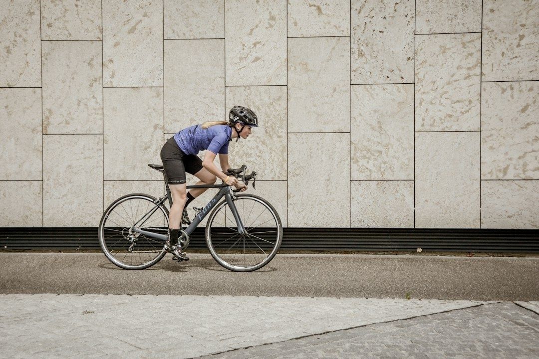 Cyklist i hjälm trampar på landsvägscykel längs en stenfasad